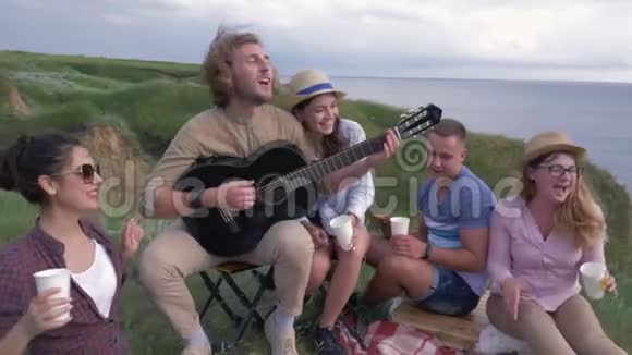 快乐的朋友一群快乐的朋友和女朋友在河边野餐时弹吉他唱歌视频的预览图