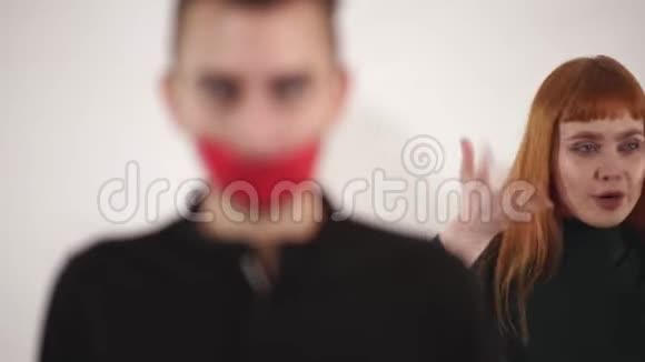 愤怒的沮丧的年轻女人红色的长发用胶带的嘴对安静的男人大喊大叫然后雄性把繁文缛节视频的预览图