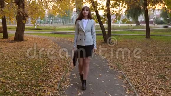 带着黑色公文包的女律师走在秋天公园的小路上视频的预览图