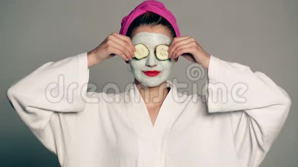 一个女孩脸上戴着面具头上戴着毛巾用灰色背景上的黄瓜遮住她的眼睛一个女人视频的预览图