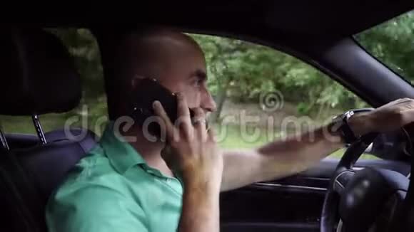 穿绿色t恤的英俊秃头在智能手机驾驶汽车上讲话视频的预览图
