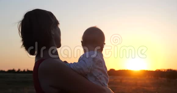 浪漫的女人手里拿着一个孩子在邋遢的田野里看日落视频的预览图