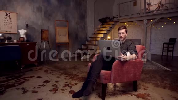 在家工作库存录像快乐的年轻英俊的男人在家里舒适的大椅子上工作视频的预览图