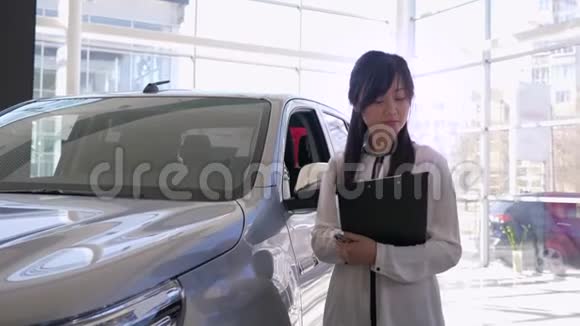 在汽车中心的新车旁微笑的女经理竖起了大拇指视频的预览图