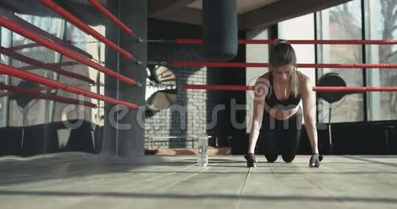 漂亮的女人在健身房里用慢动作从木地板做俯卧撑时看着摄像机视频的预览图