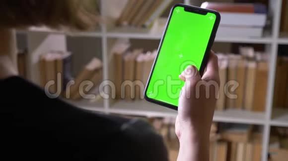 在室内图书馆用绿色彩色屏幕在手机上滚动的女学生特写后景拍摄视频的预览图