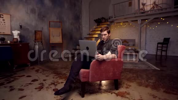 在家工作库存录像快乐的年轻英俊的男人在家里舒适的大椅子上工作视频的预览图