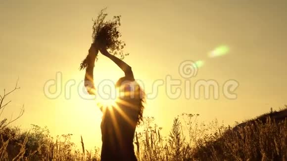 一个女孩在阳光的照耀下剪影在夏日的夕阳下挥舞着一束野花视频的预览图