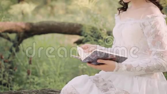 神秘的公主穿着一件白色的老式夏装正在森林里读一本书把打开的笔记本放在视频的预览图