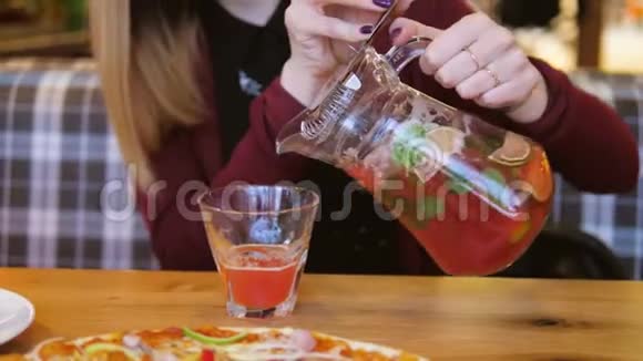 在咖啡屋的桌子上闭上女人的手把果汁从Decanter倒入玻璃杯中视频的预览图
