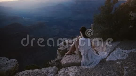 慢动作电影拍摄的兴奋年轻女子与头发吹在风中坐在史诗般的日落大峡谷视频的预览图
