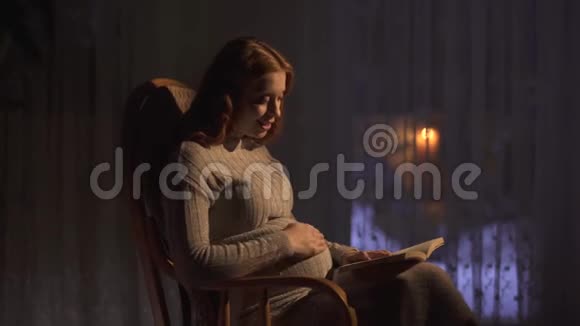 孕妇坐在黑暗的房间里的摇椅里女士大声朗读书给未出生的婴儿听视频的预览图