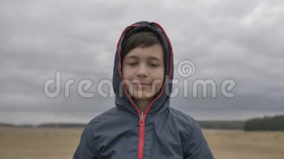 秋天户外风帽里一个滑稽的微笑男孩的肖像视频的预览图