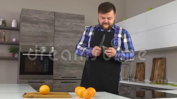 一个留着胡子的胖子正在现代化的厨房里磨一把刀在厨房里做饭前做准备动作很慢视频的预览图