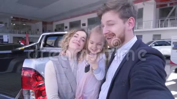 汽车中心家庭自拍父母带着可爱的带钥匙的小女孩在新家附近的手机上自拍视频的预览图