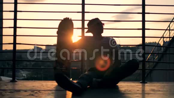 夕阳西下的城市景观年轻人坐在楼梯上用滑板降落视频的预览图
