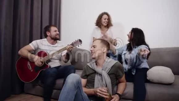 公司的4个朋友坐在沙发上听Guy弹声吉他一起玩得开心视频的预览图