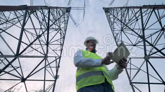 能源工人站在两座电力塔之间手里拿着一台电脑视频的预览图