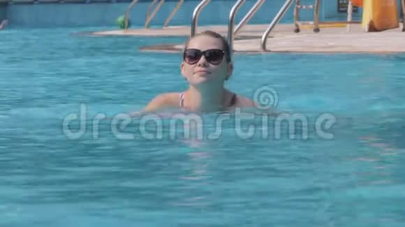 暑假期间戴太阳镜在游泳池游泳的女性肖像年轻漂亮的女孩在盆里放松假日视频的预览图
