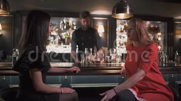 两个女朋友坐在酒吧柜台附近进行有趣的谈话背景设计中的酒保视频的预览图