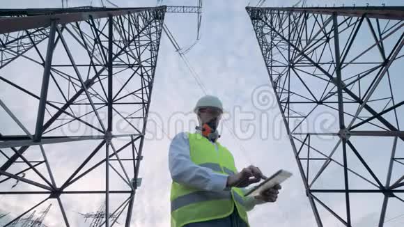 男工程师正在操作平板电脑同时站在电力线塔之间视频的预览图