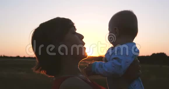 快乐的中年妇女在日落时分在田野里亲吻婴儿视频的预览图