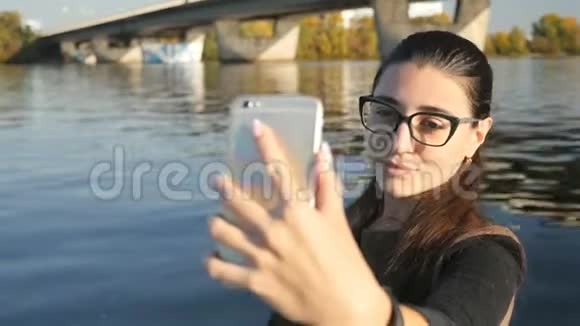 漂亮的女孩在河的背景下拍照在水边的自拍特写镜头慢慢视频的预览图