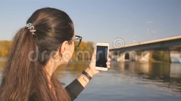 美丽的女孩拍摄大自然的照片有桥的河流风景如画在电话里拍照慢慢视频的预览图