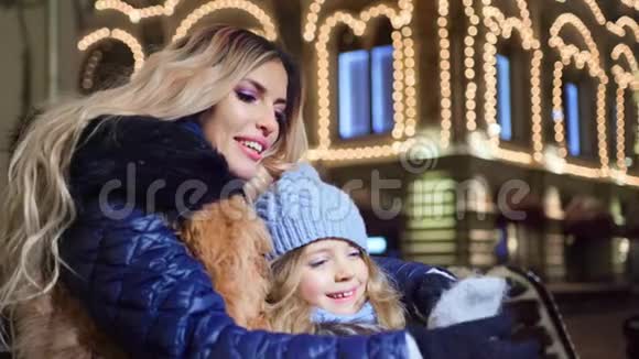 可爱的年轻母亲和微笑的女儿在街上的灯光背景下在一起玩得很开心视频的预览图
