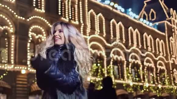美丽的女孩在户外尽情地吹着雪花在圣诞节的灿烂背景下微笑视频的预览图