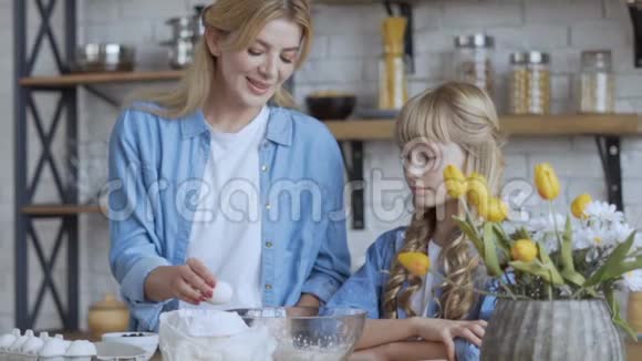 妈妈和女儿正在厨房准备一个馅饼妈妈在大碗里敲一个鸡蛋慢动作射击大型视频的预览图