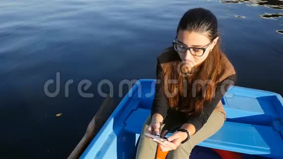漂亮的女孩坐在船上拿着电话慢动作水面上美丽的波浪视频的预览图