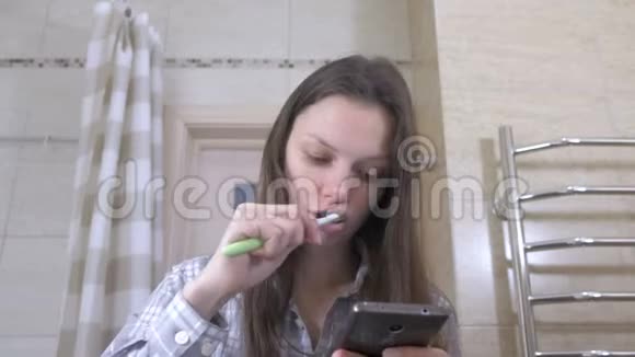 女人在浴室刷牙看着手机里的视频视频的预览图
