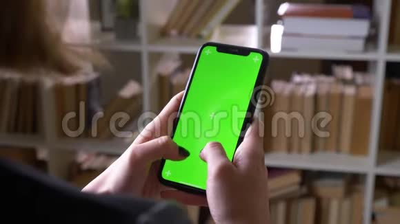 在室内图书馆用绿色彩色屏幕在手机上发短信的女学生特写后景拍摄视频的预览图