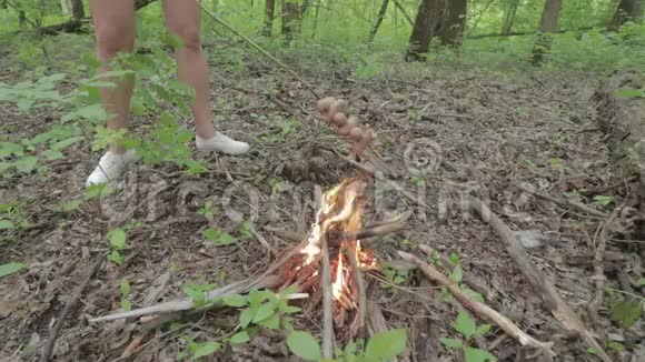 在一个春天的森林里一个女孩在篝火旁的棍子上烤香肠视频的预览图