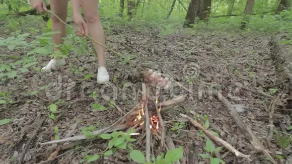在春天森林的篝火上女孩在棍子上烤香肠视频的预览图