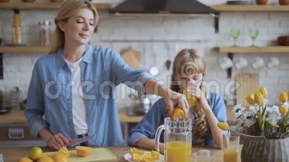 妈妈和女儿在厨房里做天然橙汁迷人的年轻妈妈把橙汁挤成一团视频的预览图