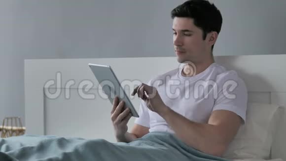 床上青年男子平板电脑在线视频聊天视频的预览图