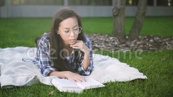 可爱的混血女人躺在校园附近的格子和草地上视频的预览图