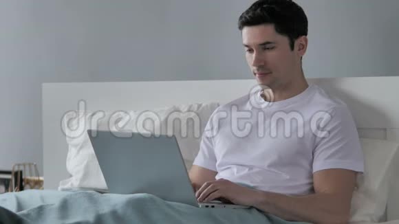 年轻人在床上工作时庆祝成功视频的预览图