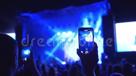 摇滚音乐会歌迷们在手机上拍摄在夜晚明亮的灯光下表演音乐团体视频的预览图