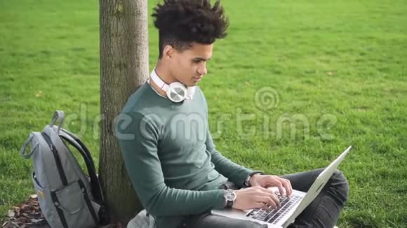非裔美国学生在坐在草地上的笔记本电脑上打字视频的预览图