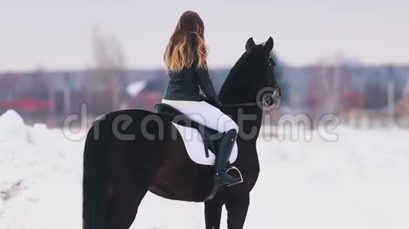 一个快乐的年轻女子长发在一个村庄骑马站在雪地上视频的预览图