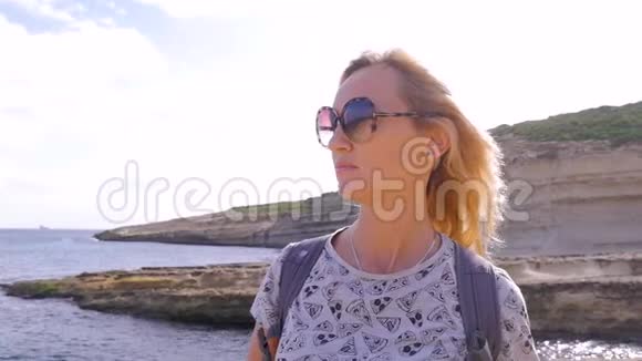 戴着眼镜的漂亮中年金发旅游女郎和一件带披萨的可爱有趣的t恤站在岩石上视频的预览图