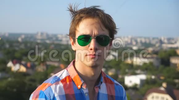 一位戴墨镜的年轻人坐在高楼大厦屋顶上的特写肖像背景是城市景观视频的预览图