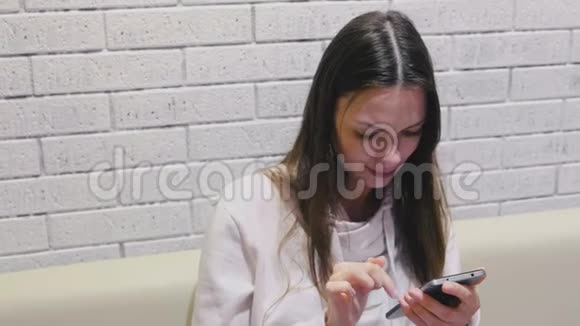 美丽的黑发微笑的女人正在打字并在手机上搜索一条信息坐在咖啡馆里等人视频的预览图