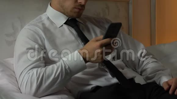 一个人躺在床上在工作了很长一天后在智能手机上看新闻和电子邮件视频的预览图