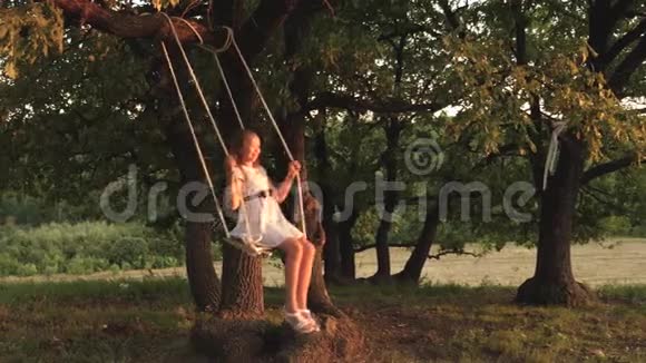 快乐的童年概念孩子们骑着绳子在森林里的橡树树枝上摇摆女孩笑高兴年轻女孩视频的预览图