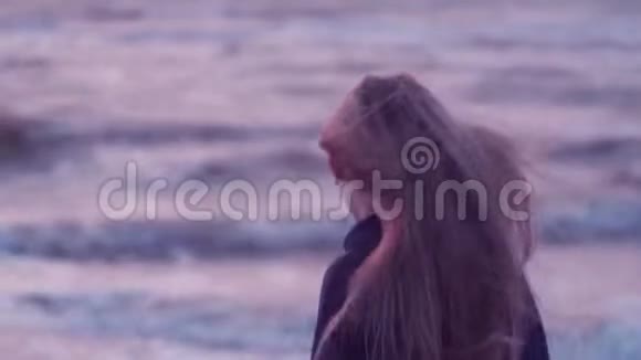美丽的女孩看着大海转过相机她的头发在背景下发展风波浪视频的预览图
