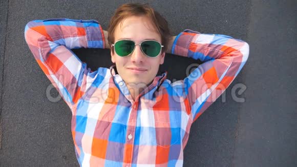 一个年轻快乐的男人戴着太阳镜躺在高楼大厦的屋顶上微笑着穿衬衫的帅哥视频的预览图